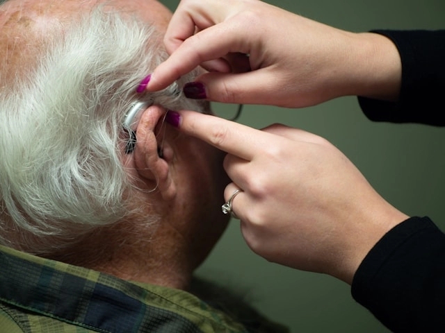 Close-up of a person fitting a hearing aid in a man's ear