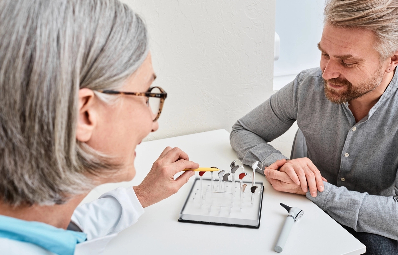 Female audiologist offers BTE hearing aids to man patient with hearing problems for treatment his deafness.