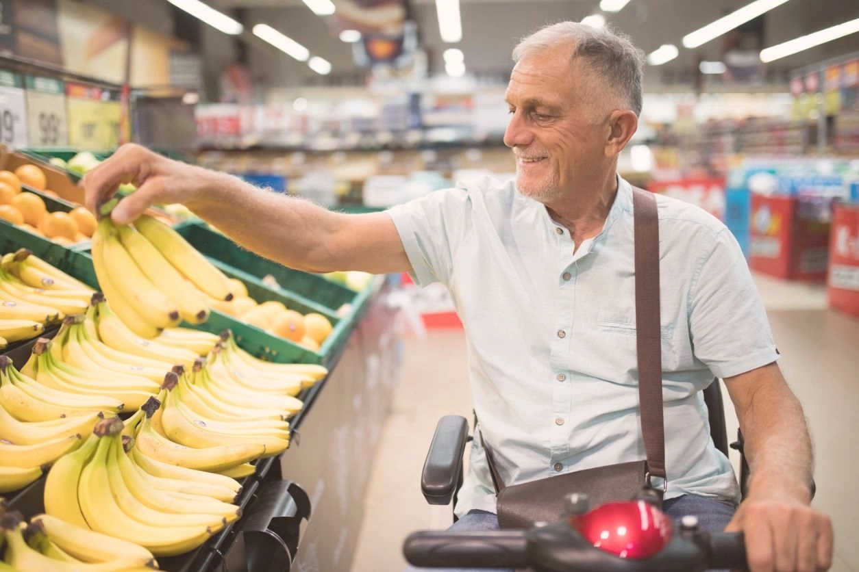 A man selecting bananas at a supermarket in a mobility scooter