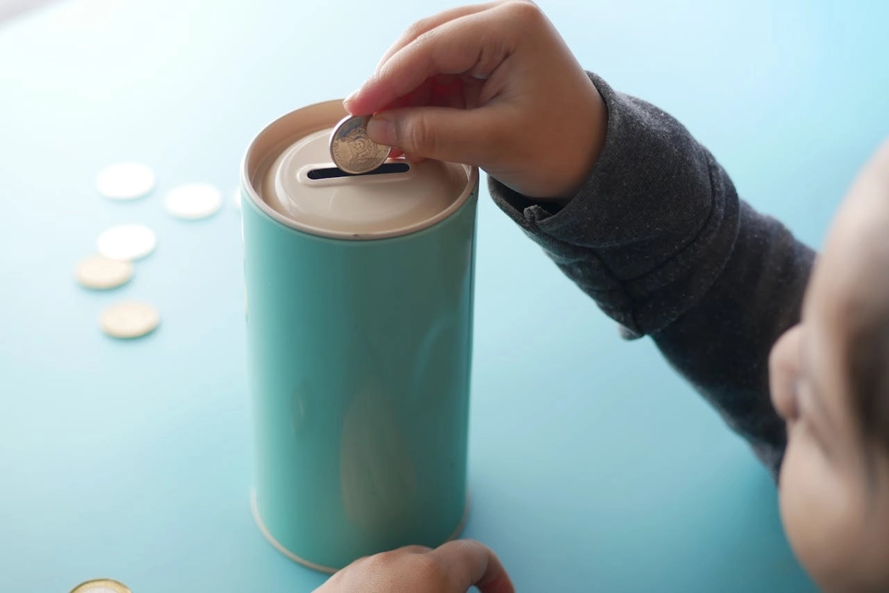 A kids hand dropping coins into a piggybank